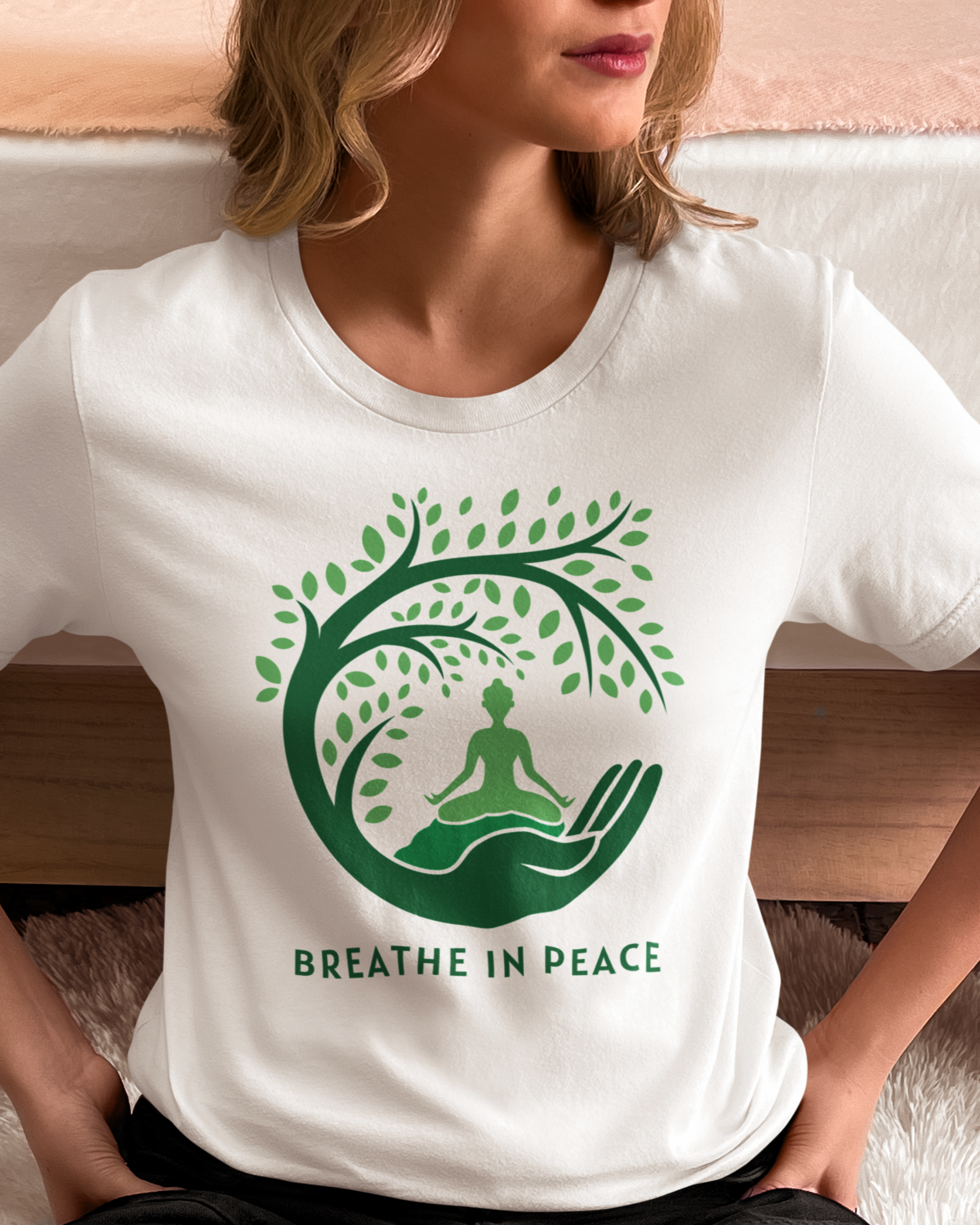 Person wearing a white t-shirt with a green tree and meditation design, sitting on a couch.