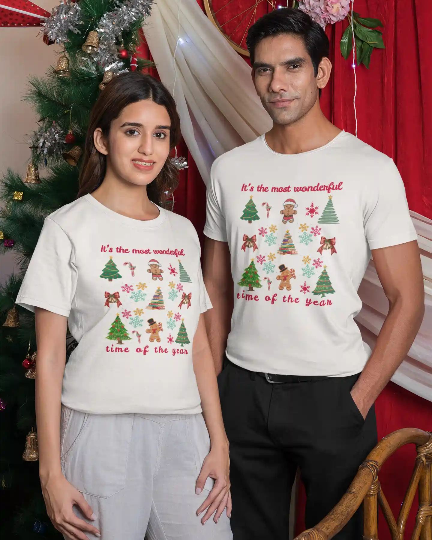 Two people wearing Christmas-themed t-shirts with a decorated Christmas tree in the background.