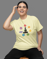 Person wearing a light yellow t-shirt with a colorful design, sitting on a wooden stool against a gray background.