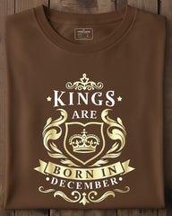 Brown t-shirt with gold 'Kings are born in December' design on a wooden surface