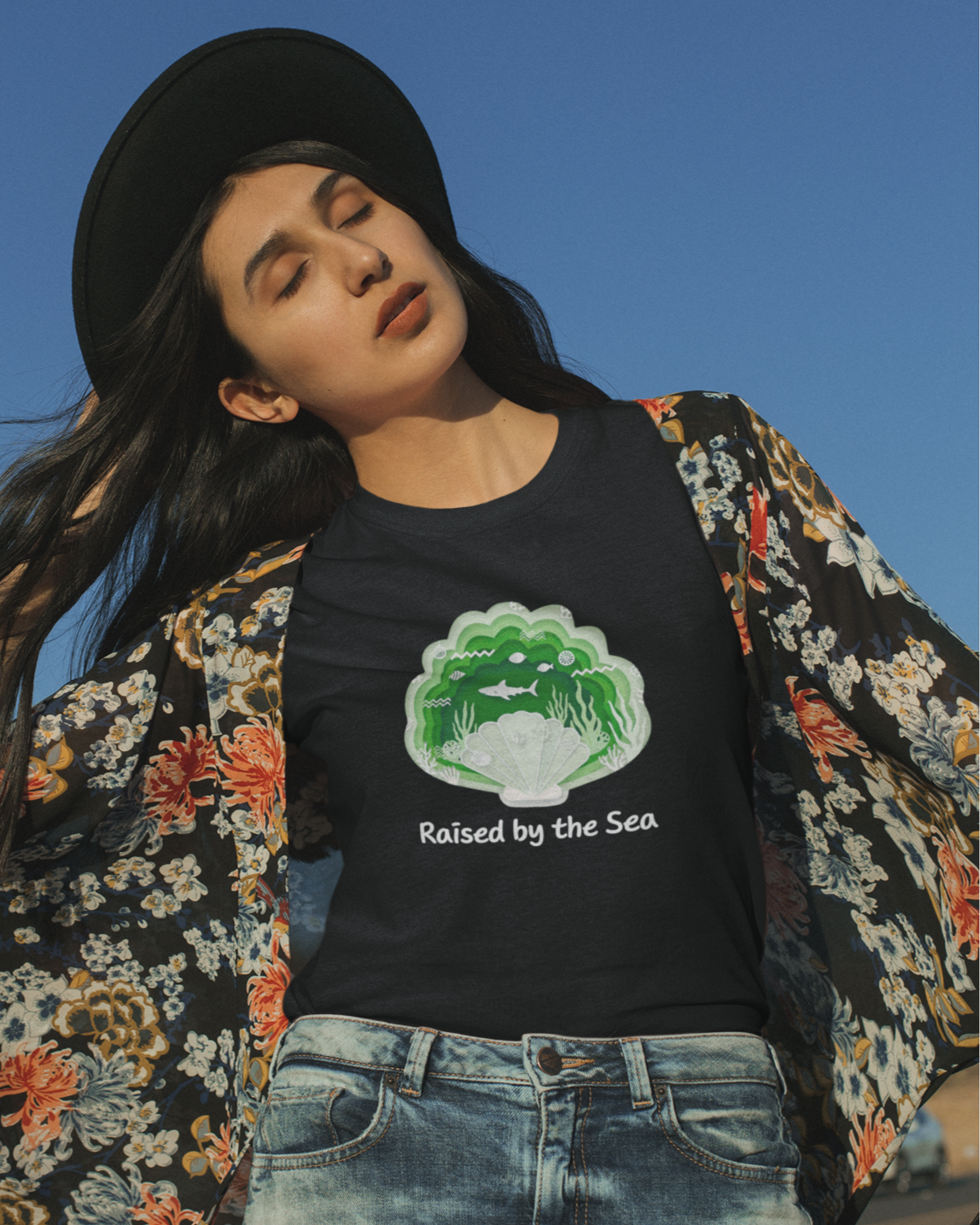 Woman wearing a black t-shirt with a graphic design and text, standing outdoors against a clear blue sky.