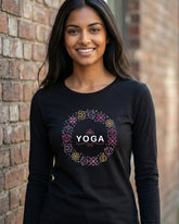 Woman wearing a black long-sleeve shirt with 'Yoga' design against a brick wall.