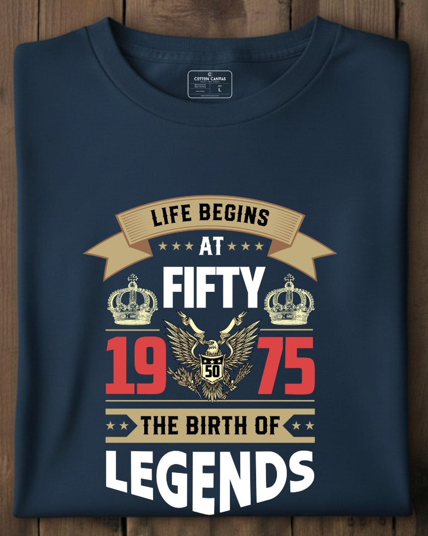 Navy blue t-shirt with 'Life Begins at Fifty 1975 The Birth of Legends' design on a wooden surface