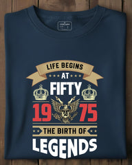 Navy blue t-shirt with 'Life Begins at Fifty 1975 The Birth of Legends' design on a wooden surface