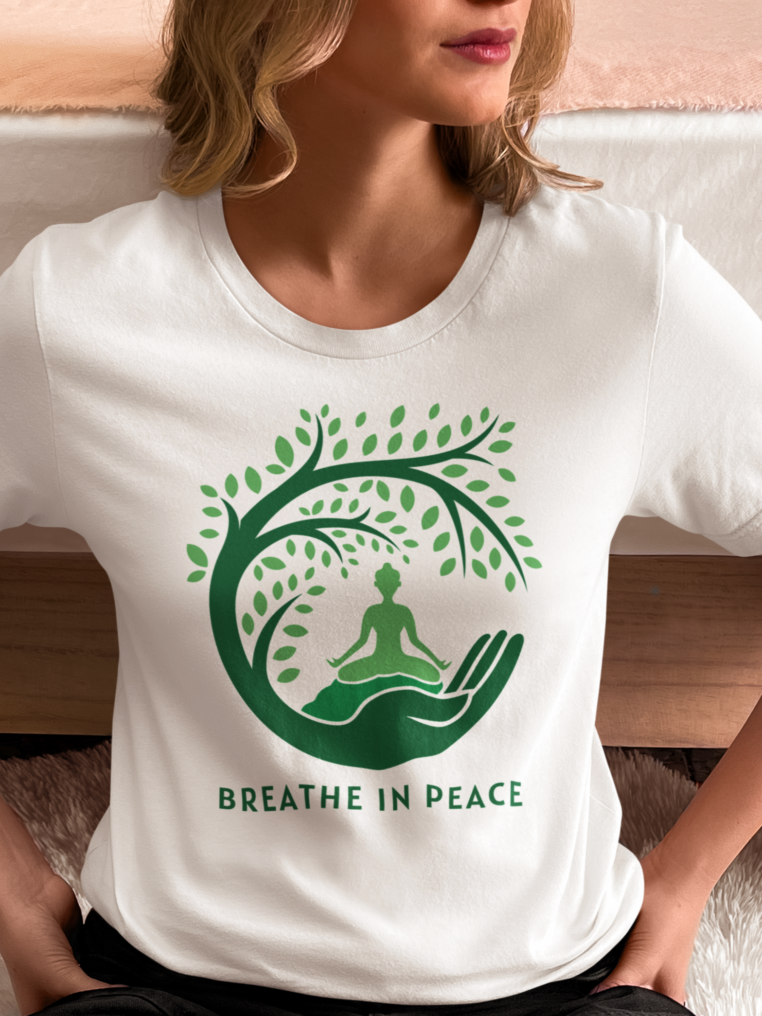 Person wearing a white t-shirt with a green tree and meditation design, sitting on a couch.