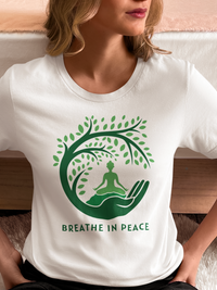 Person wearing a white t-shirt with a green tree and meditation design, sitting on a couch.