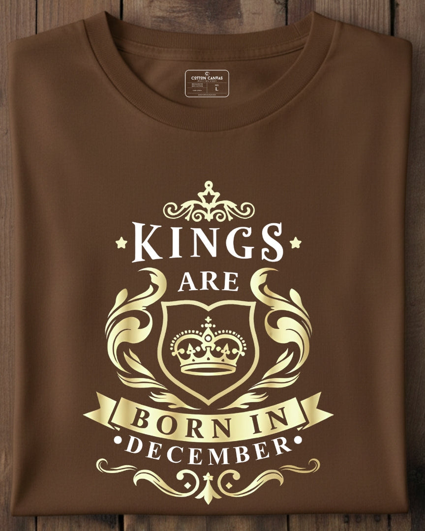Brown t-shirt with gold 'Kings are born in December' design on a wooden surface