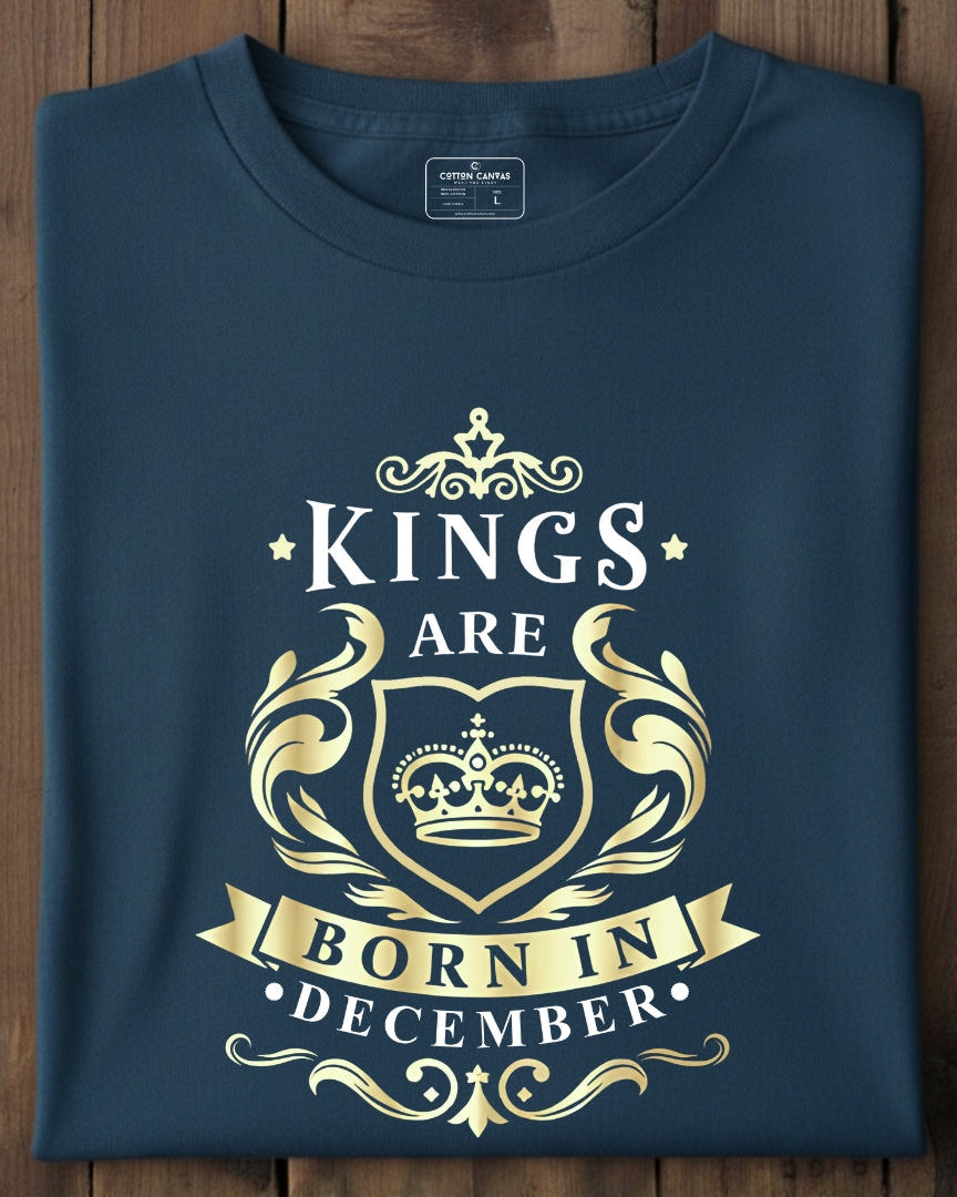 Folded navy blue t-shirt with gold 'Kings are born in December' text on a wooden surface