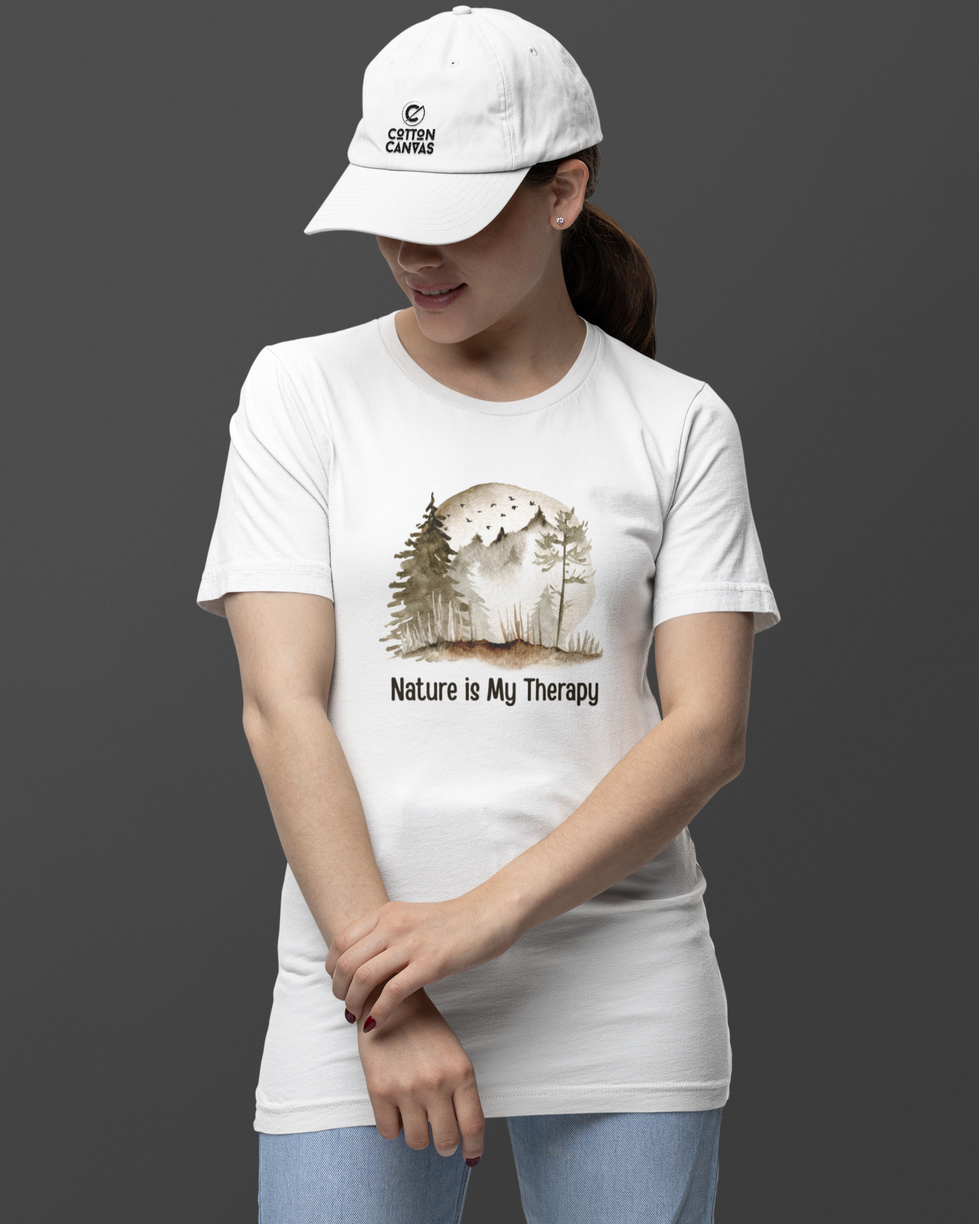 Person wearing a white t-shirt with a nature-themed design and a cap on a dark background