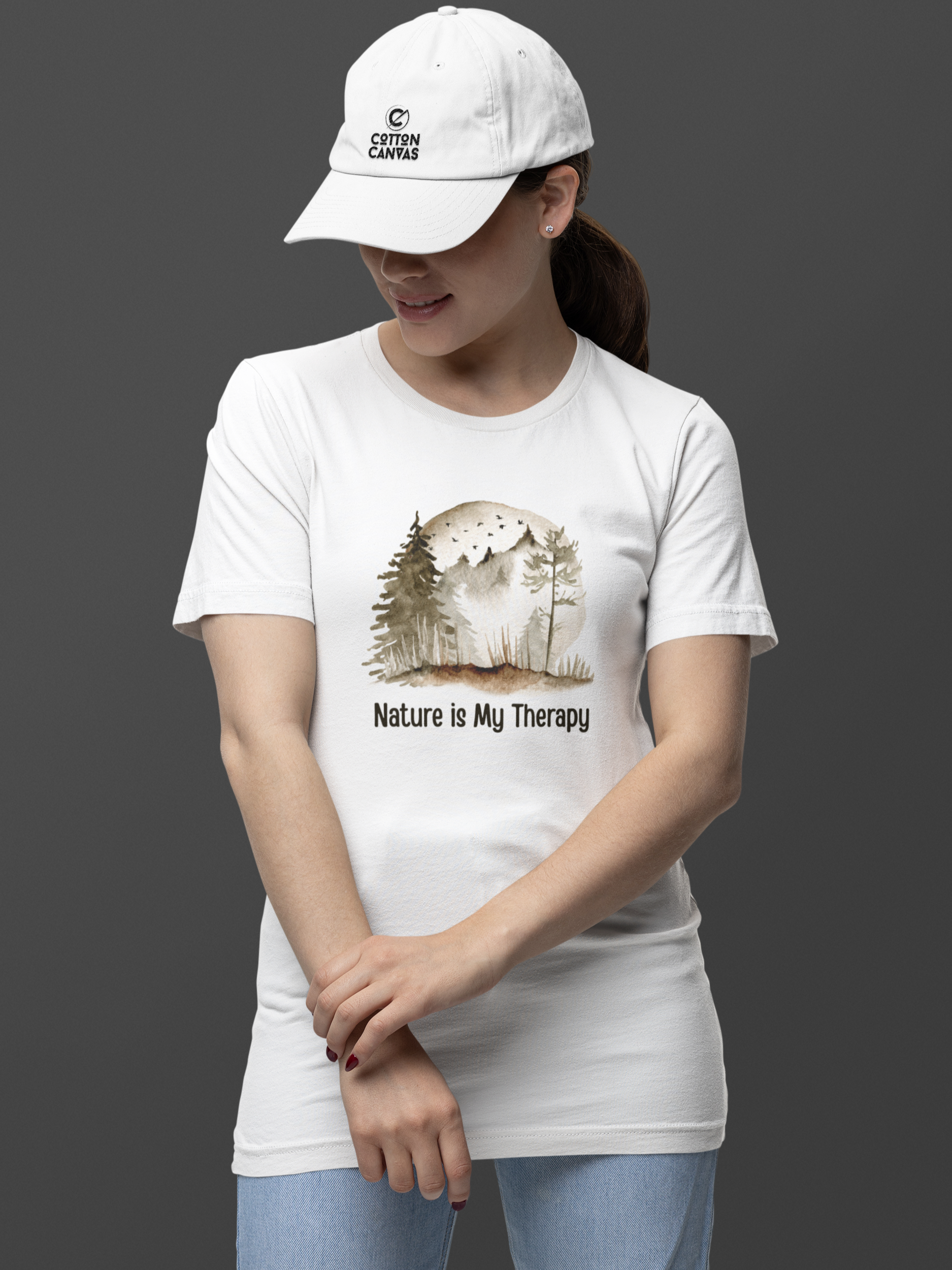 Person wearing a white t-shirt with a nature-themed design and a cap on a dark background